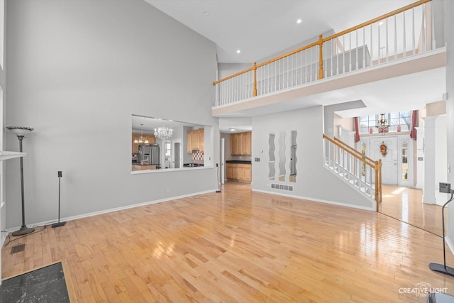 unfurnished living room featuring light wood finished floors, visible vents, baseboards, stairs, and an inviting chandelier