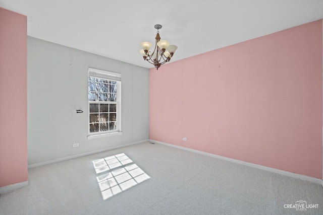 carpeted spare room featuring an inviting chandelier and baseboards