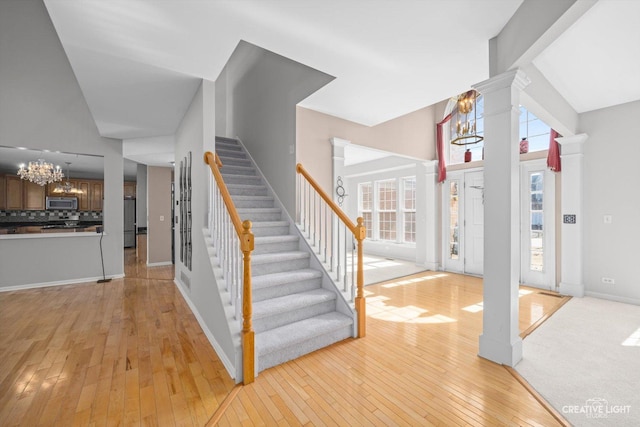 interior space featuring baseboards, wood-type flooring, a notable chandelier, and ornate columns