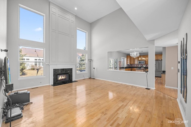 living area featuring baseboards, light wood-type flooring, a high end fireplace, and a chandelier