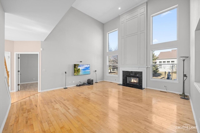 unfurnished living room with a fireplace, baseboards, a high ceiling, and light wood-style floors