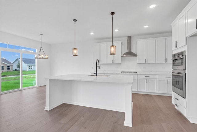 kitchen featuring white cabinets, a kitchen island with sink, sink, and wall chimney range hood