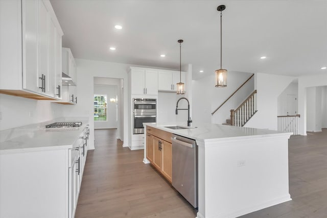 kitchen featuring sink, appliances with stainless steel finishes, a kitchen island with sink, white cabinetry, and hanging light fixtures