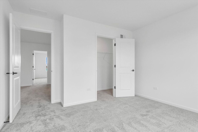 unfurnished bedroom featuring a walk in closet, light colored carpet, and a closet