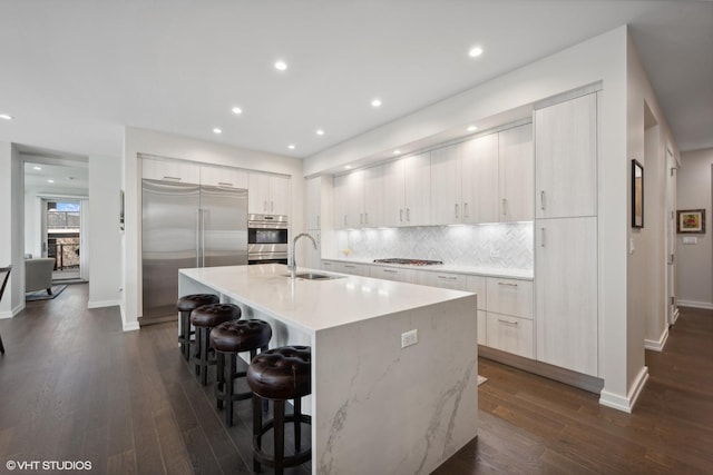 kitchen with a kitchen bar, sink, appliances with stainless steel finishes, a kitchen island with sink, and backsplash