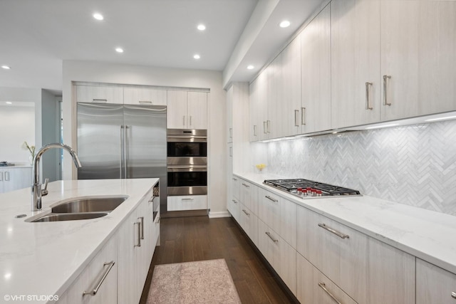 kitchen with sink, appliances with stainless steel finishes, dark hardwood / wood-style floors, light stone countertops, and backsplash