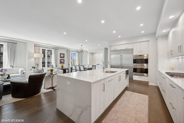 kitchen with a large island, sink, dark wood-type flooring, appliances with stainless steel finishes, and white cabinetry