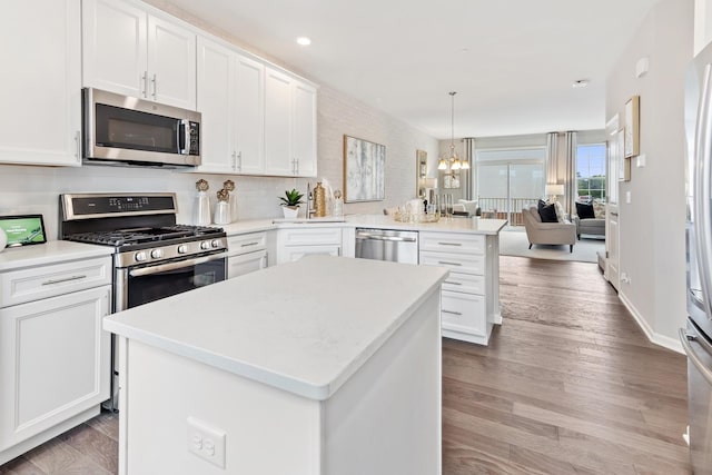 kitchen featuring white cabinetry, decorative light fixtures, appliances with stainless steel finishes, kitchen peninsula, and a kitchen island