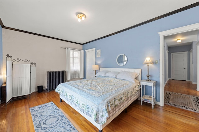 bedroom with radiator, baseboards, wood finished floors, and ornamental molding