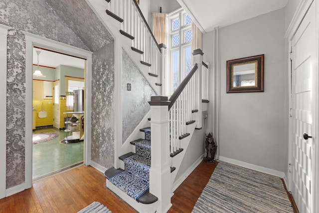 staircase with wallpapered walls, wood-type flooring, and baseboards