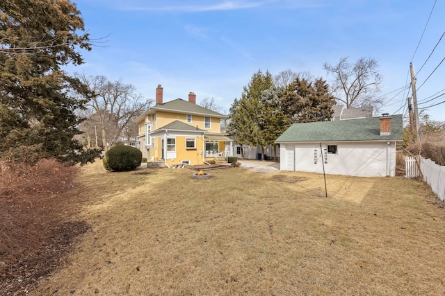 rear view of house with a chimney, an outdoor structure, fence, and a lawn