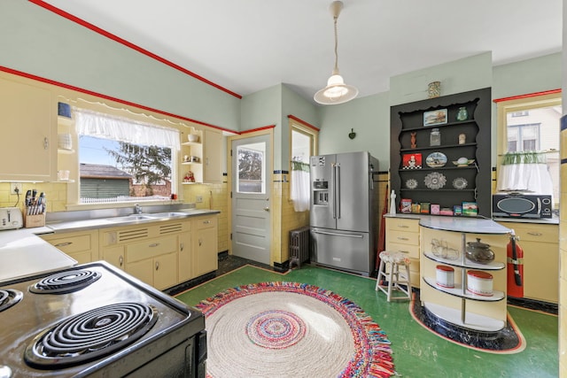 kitchen with electric stove, stainless steel fridge with ice dispenser, stainless steel countertops, dark floors, and a sink