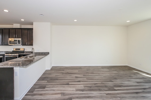 kitchen featuring appliances with stainless steel finishes, sink, dark stone countertops, dark brown cabinetry, and light hardwood / wood-style flooring