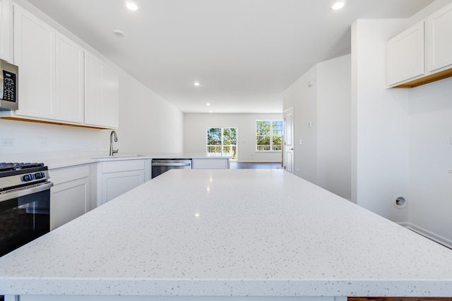 kitchen with sink, white cabinetry, appliances with stainless steel finishes, a kitchen island, and light stone countertops