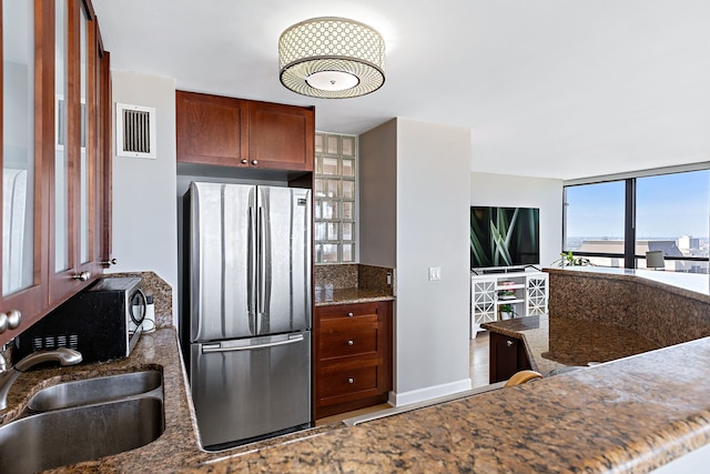 kitchen featuring dark stone countertops, sink, and stainless steel fridge