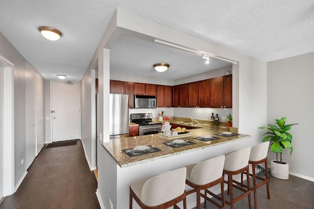 kitchen with appliances with stainless steel finishes, dark hardwood / wood-style flooring, light stone countertops, and kitchen peninsula