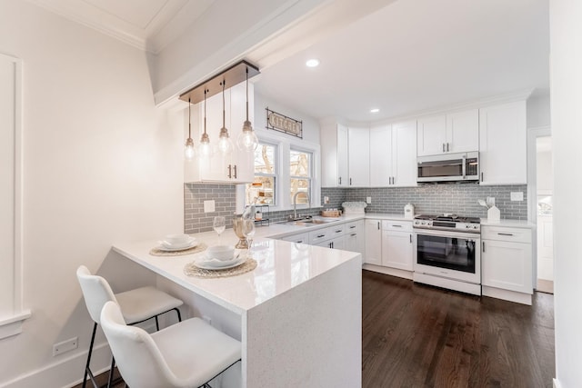 kitchen with sink, appliances with stainless steel finishes, white cabinetry, a kitchen breakfast bar, and decorative light fixtures