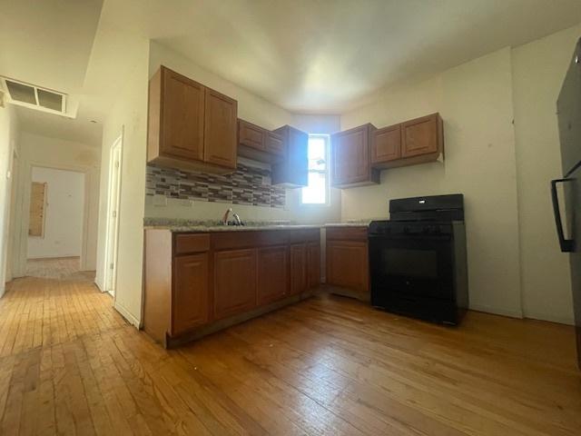 kitchen with backsplash, black range, and light hardwood / wood-style floors