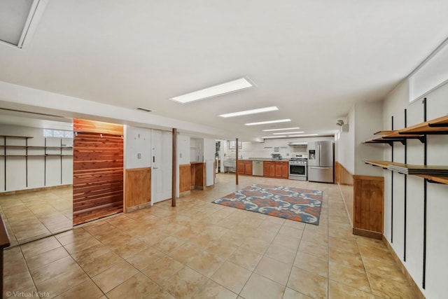 interior space featuring light tile patterned floors, wood walls, extractor fan, and appliances with stainless steel finishes