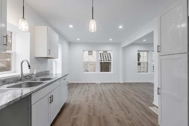 kitchen with white cabinetry, sink, light wood-type flooring, and decorative light fixtures