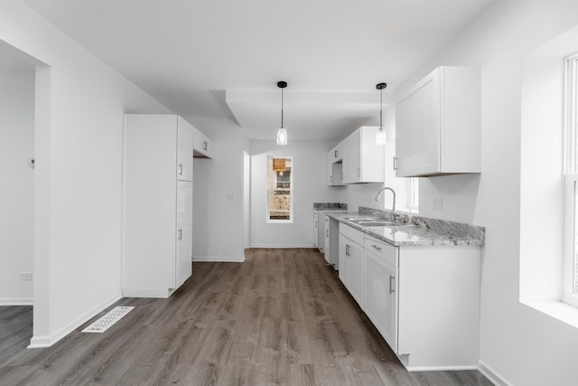 kitchen with pendant lighting, sink, light hardwood / wood-style flooring, white cabinetry, and light stone counters