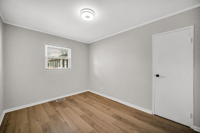 empty room with visible vents, crown molding, baseboards, and wood finished floors