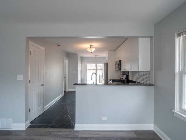 kitchen featuring appliances with stainless steel finishes, tasteful backsplash, white cabinetry, sink, and kitchen peninsula