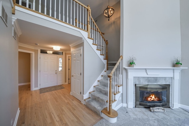 foyer entrance featuring crown molding, a towering ceiling, a tile fireplace, and light wood-type flooring