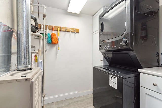 washroom with heating unit, stacked washer / drying machine, light hardwood / wood-style flooring, and cabinets