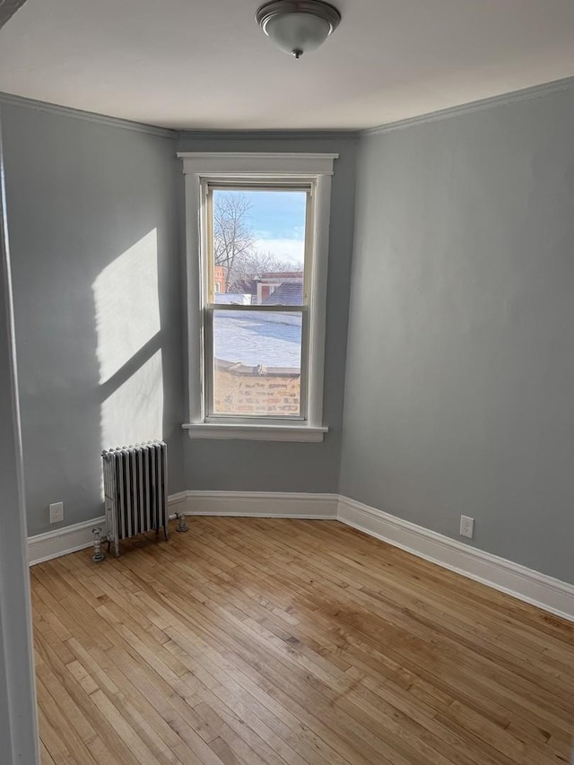 empty room featuring crown molding, radiator heating unit, and light hardwood / wood-style floors