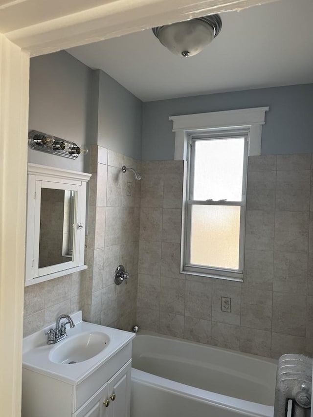 bathroom featuring radiator heating unit, tiled shower / bath combo, vanity, and tile walls