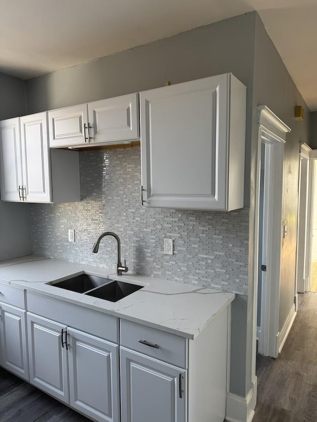 kitchen with white cabinetry, sink, backsplash, light stone countertops, and dark wood-type flooring