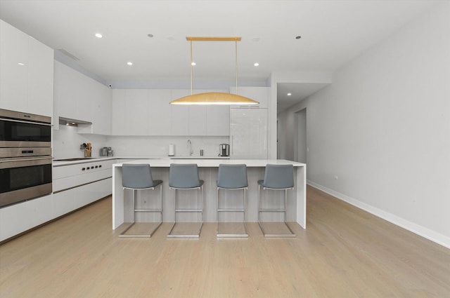 kitchen with a breakfast bar area, white cabinetry, decorative light fixtures, light hardwood / wood-style floors, and decorative backsplash