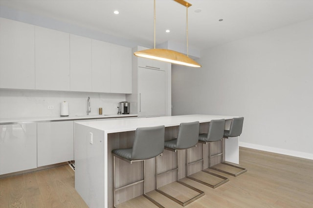 kitchen with white cabinetry, sink, pendant lighting, and light hardwood / wood-style flooring