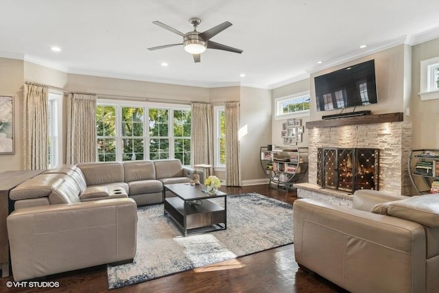 living room with dark wood-type flooring, ceiling fan, a fireplace, and crown molding