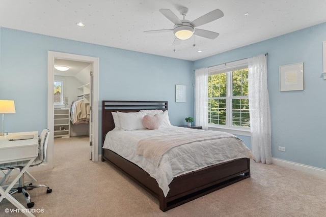 carpeted bedroom with a walk in closet and ceiling fan