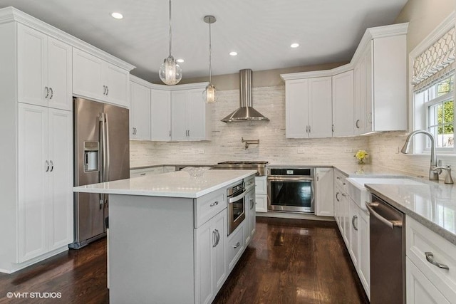 kitchen with sink, white cabinetry, stainless steel appliances, a kitchen island, and wall chimney exhaust hood