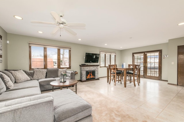 tiled living room with french doors, ceiling fan, and a stone fireplace