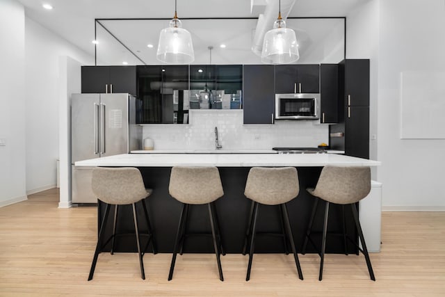 kitchen featuring pendant lighting, stainless steel appliances, a kitchen island, decorative backsplash, and light wood-type flooring