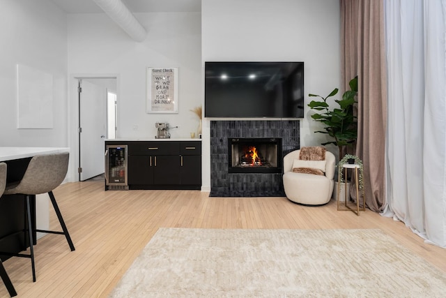 living room featuring wine cooler, bar, a tiled fireplace, and light wood-type flooring