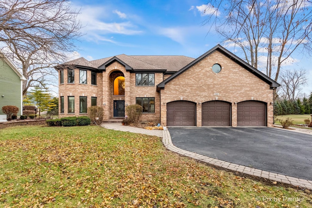 traditional-style house with a shingled roof, a front lawn, a garage, aphalt driveway, and brick siding