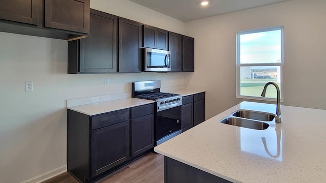 kitchen with sink, appliances with stainless steel finishes, light stone counters, dark brown cabinetry, and light wood-type flooring