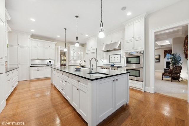 kitchen featuring sink, a center island with sink, hanging light fixtures, stainless steel appliances, and white cabinets