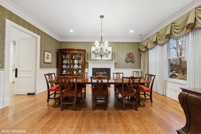 dining space featuring a notable chandelier, crown molding, a fireplace, and light wood-type flooring