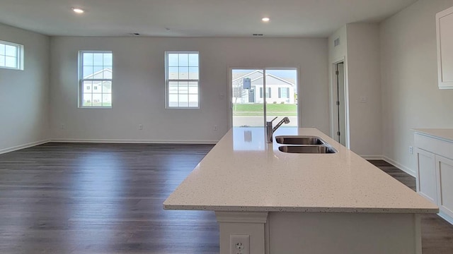 kitchen with an island with sink, light stone countertops, sink, and white cabinets