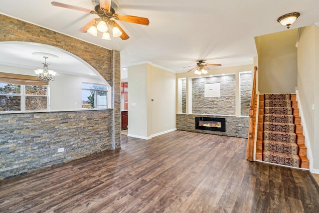 unfurnished living room featuring wood finished floors, a fireplace, arched walkways, stairs, and ceiling fan with notable chandelier