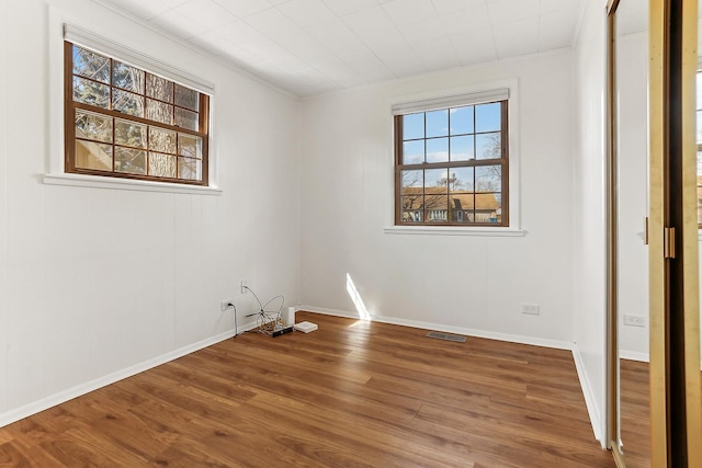 unfurnished room with baseboards, visible vents, wood finished floors, and ornamental molding