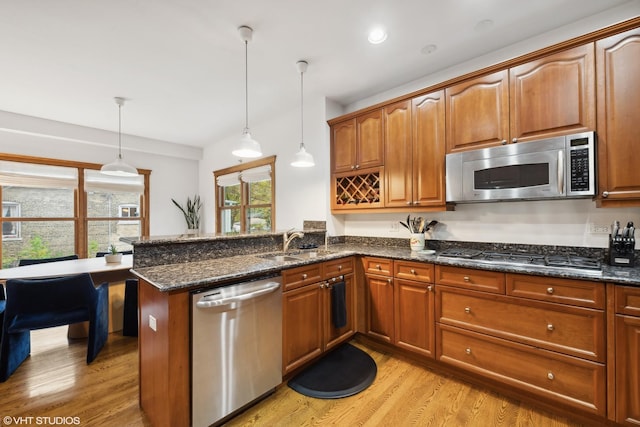 kitchen with stainless steel appliances, light hardwood / wood-style flooring, sink, dark stone countertops, and pendant lighting