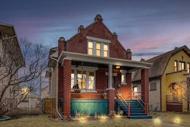 view of front of house with fence, a gate, brick siding, and covered porch