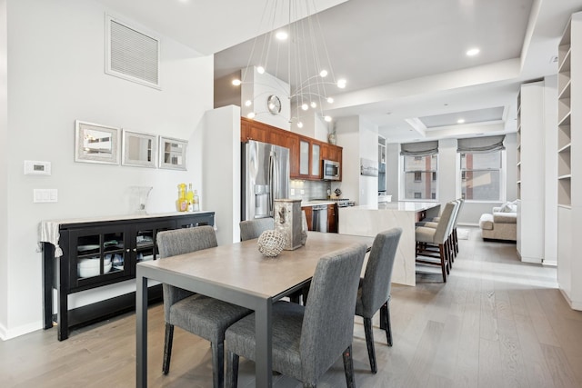 dining space featuring a notable chandelier, a raised ceiling, and light wood-type flooring